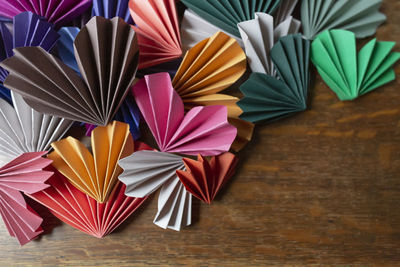 Many colored origami paper valentine hearts arranged on wooden surface