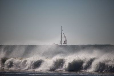 Wave splashing in sea with sailboat against clear sky