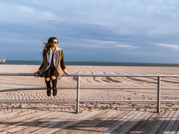 Full length of woman standing on railing against sea