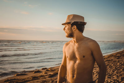 Man standing at beach against sky during sunset