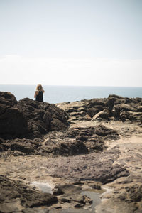 Rear view of woman at rocky shore against clear sky