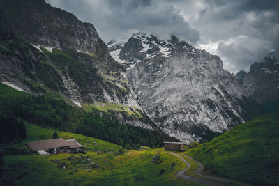 Scenic view of snowy mountains with winding road and cottage in valley against sky