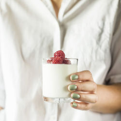 Midsection of woman holding yogurt and raspberries in drinking glass