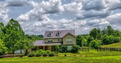 House on field by trees against sky