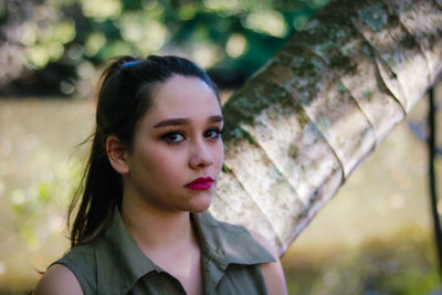 Close-up portrait of young woman standing by tree