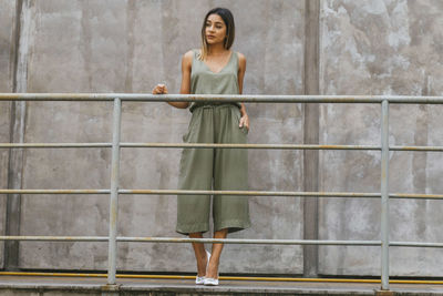 Full length of fashionable young woman standing by railing against concrete wall