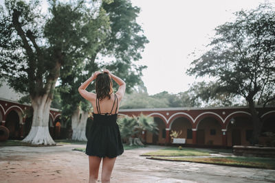 Rear view of woman standing by trees against sky