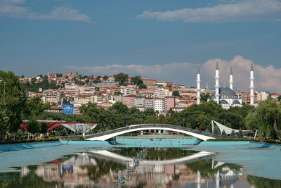 Bridge over river by buildings in city against sky