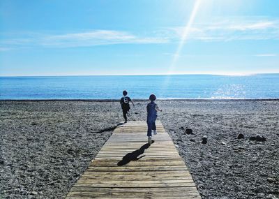 Rear view of children running at beach during sunny day