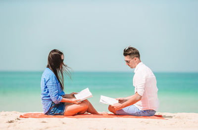 People sitting on beach by sea against sky