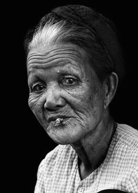 Portrait of senior woman smoking cigarette against black background