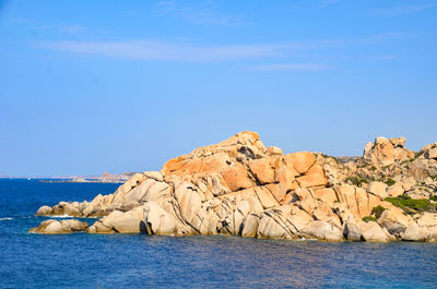 Rock formations by sea against blue sky