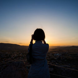 Rear view of woman standing at observation point against clear sky at sunset