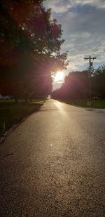 Road by trees against sky during sunset