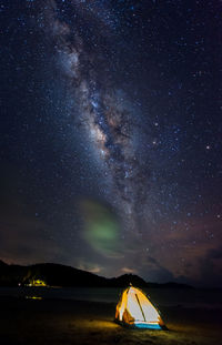 Illuminated tent at beach against sky at night