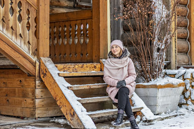 Warmly dressed young woman posing on the porch of a wooden house in the village. winter 