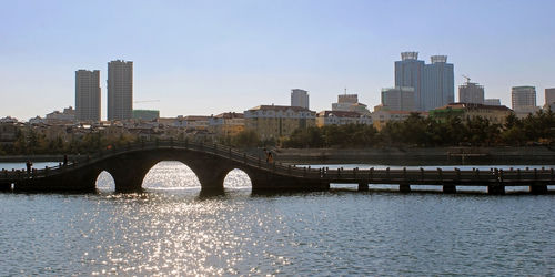 Bridge over river by buildings against sky in city