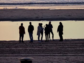 Silhouette people on beach against sky during sunset