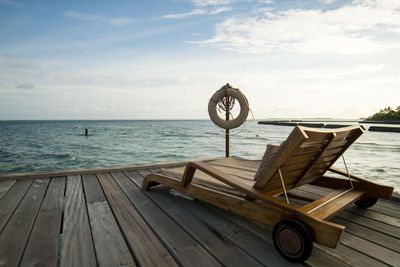 Deck chair on sea shore against sky