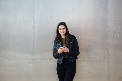 Portrait of smiling young woman standing against metallic wall