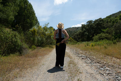 Young man walking through the mountain with flowers behind his back