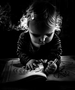 Close-up of cute toddler girl drawing on book in darkroom