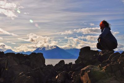 Woman crouching on rock against sky