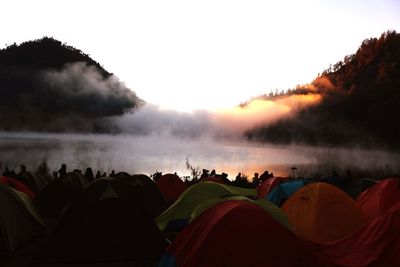 Group of people camping at lake against sky during sunset