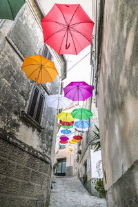 Low angle view of multi colored umbrellas hanging on alley amidst buildings