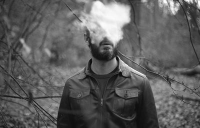 Man exhaling smoke while standing in forest