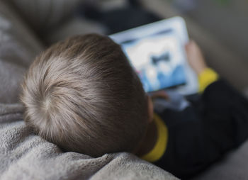 High angle view of boy using tablet computer while sitting on sofa at home