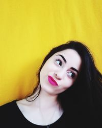 Young beautiful woman with pink lipstick and long hair against yellow wall