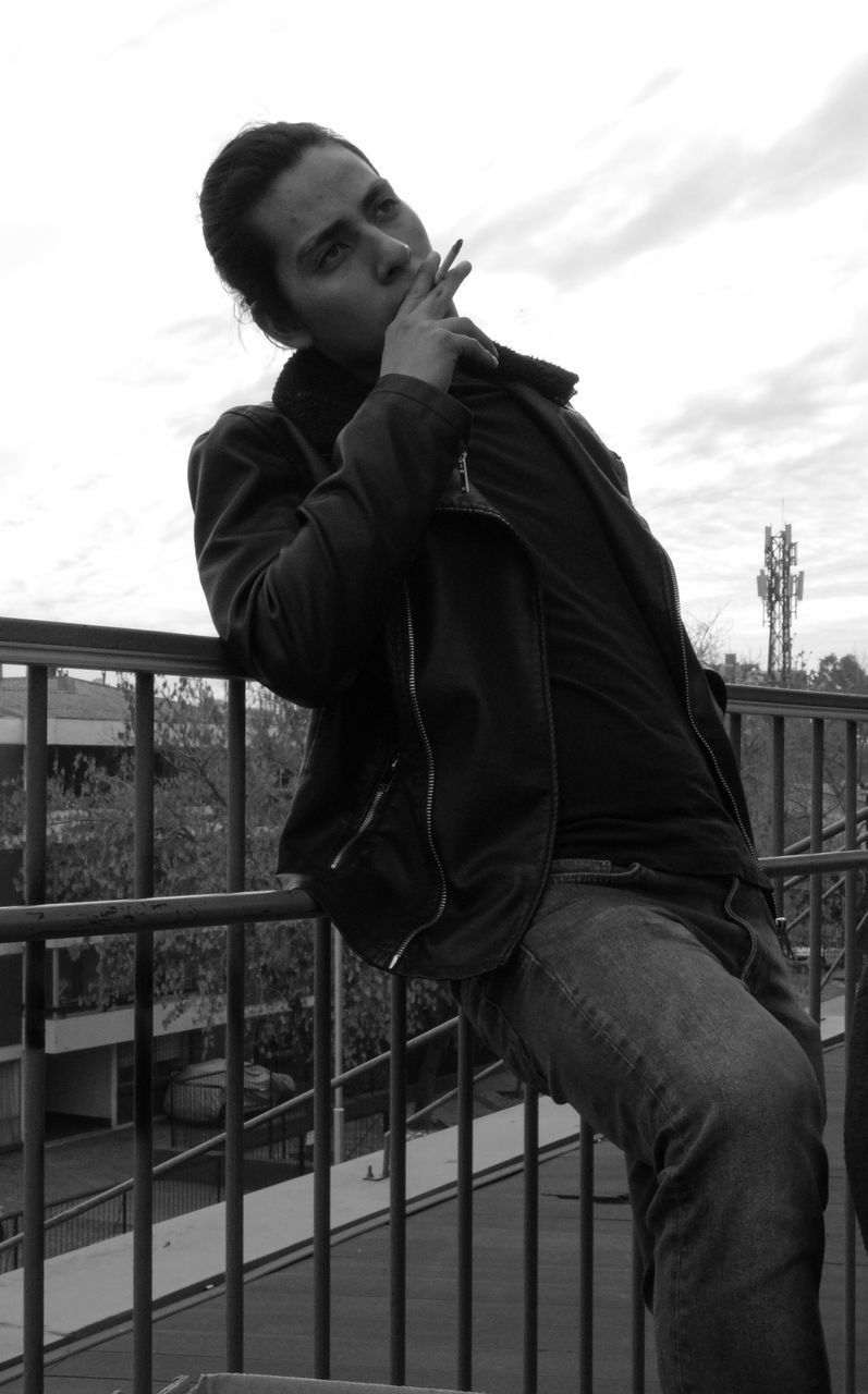 FULL LENGTH OF YOUNG MAN LOOKING AWAY WHILE STANDING AGAINST RAILING