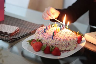 Close-up of hand lighting candles on cake