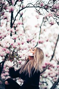 Low angle view of woman and pink cherry blossom tree
