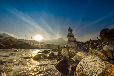 Low angle view of stones stacked by river against sky