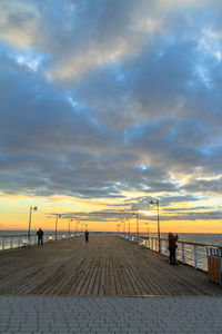 Boardwalk over sea against cloudy sky during sunset