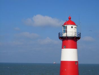 Red lighthouse by sea against sky