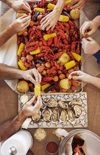 Overhead view of people eating a crayfish boil with potatoes, corns and oysters at dining table