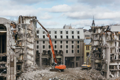 Red excavator with long mechanical arm at height breaks off pieces of the house.