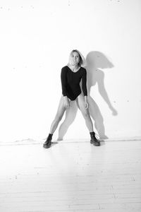 Full length portrait of young woman dancing against wall