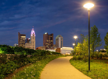 Illuminated street amidst buildings against sky at night