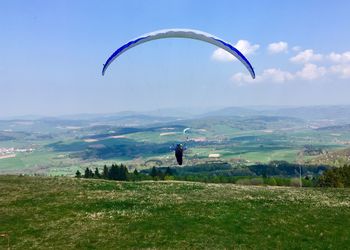 Person paragliding on field against sky