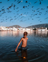 Full length of shirtless boy in water against sky