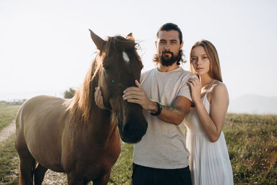 Couple standing by horse on land against sky