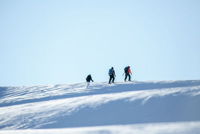 People skiing on snowcapped mountain against clear sky