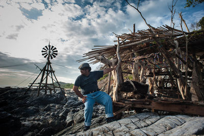 Full length of man sitting by hut on rocky coastline