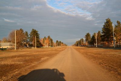 Road by trees on field against sky