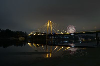 Illuminated bridge over river against sky at night