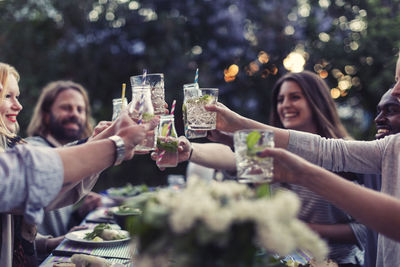 Multi-ethnic friends toasting mojito glasses at dinner table in yard